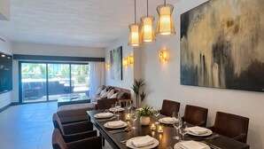 A modern dining area with a long table set for six, surrounded by chairs, with pendant lights above and a large abstract painting on the wall. - Master Suite with private Pool in Aldea Thai (Playa del Carmen)