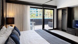 A modern hotel room with a large bed, a TV, and a balcony with a view of buildings and greenery. - Master Suite with private Pool in Aldea Thai (Playa del Carmen)