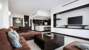 A modern living room with a sofa, ottoman, and a coffee table. There is a kitchen area in the background with a dining set. - Master Suite with private Pool in Aldea Thai (Playa del Carmen)