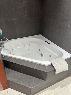 Une salle de bain moderne avec une baignoire sur pieds, des murs recouverts de carreaux foncés et un porte-serviettes apparent.