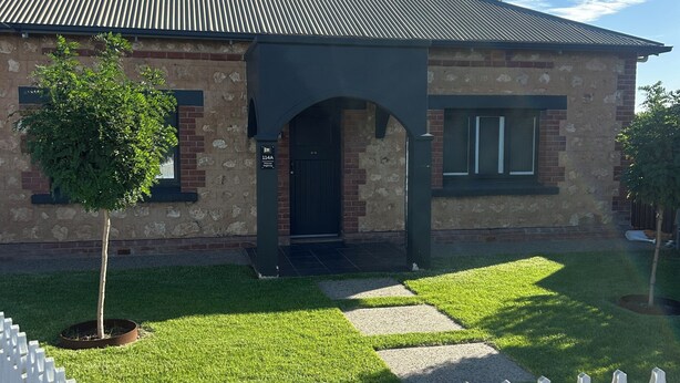 A two-story house with a brick facade, a metal roof, and a white picket fence.