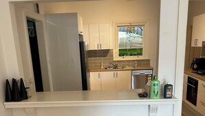 A kitchen with a white island, two stools, a refrigerator, and a window with a view.