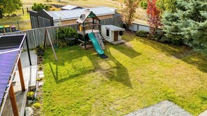 A fenced backyard with a wooden playhouse, a slide, and a small deck. - No. 52 | A2O at your backdoor + Playground & BBQ (Twizel)