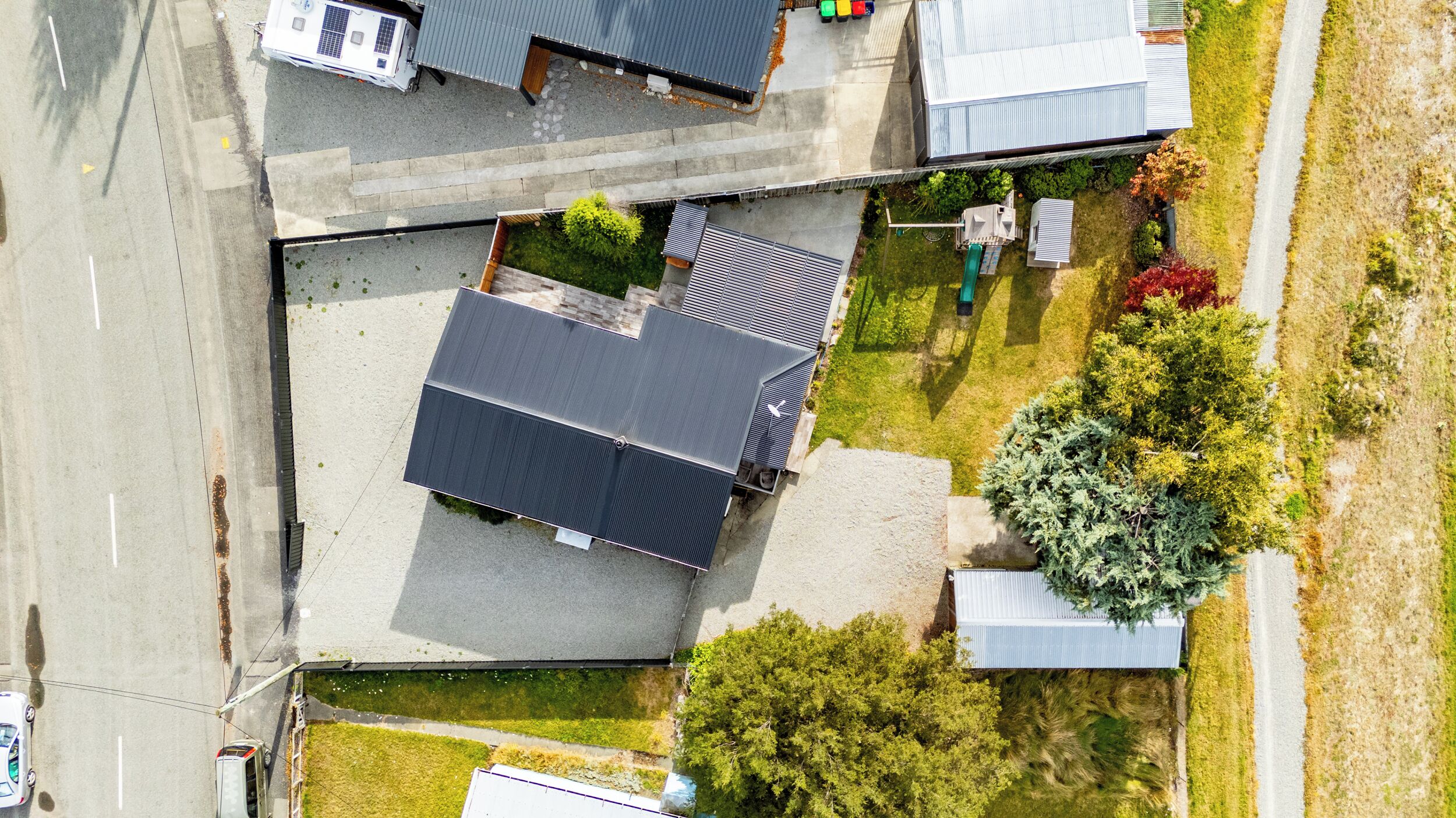 An aerial view of a residential area with a house featuring a sloped roof, a driveway, and a small garden with various plants.