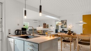 Uma cozinha moderna com ilha central, área de refeições com mobiliário de madeira e sala de estar com sofá e mesa de centro.