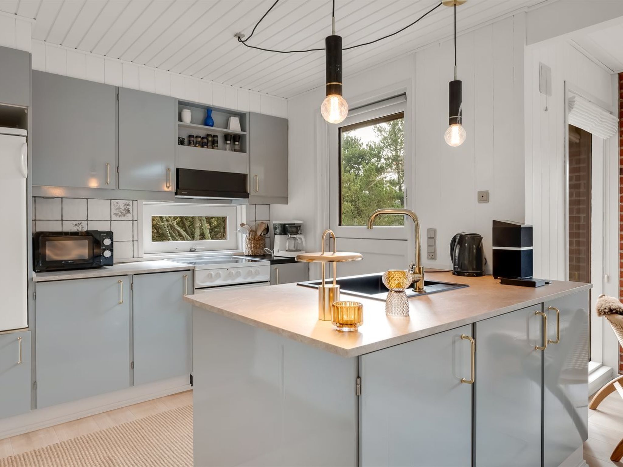 Une cuisine moderne dotée d’un îlot central, d’appareils électroménagers intégrés et de luminaires suspendus.