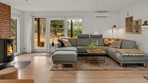 Uma sala de estar moderna com lareira, sofá em curva, mesa de centro e uma janela grande com vista para árvores.