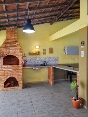A kitchen with a brick oven, a hanging light fixture, a tiled backsplash, and a potted plant. - Beautiful house with barbecue, gourmet area, garage, 4 minutes from the beach. (Armação dos Búzios)