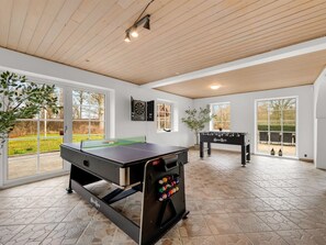 Zona interior àmplia amb taula de futbolí, taula de ping-pong i tirallengas, amb grans finestres i sostre de fusta.