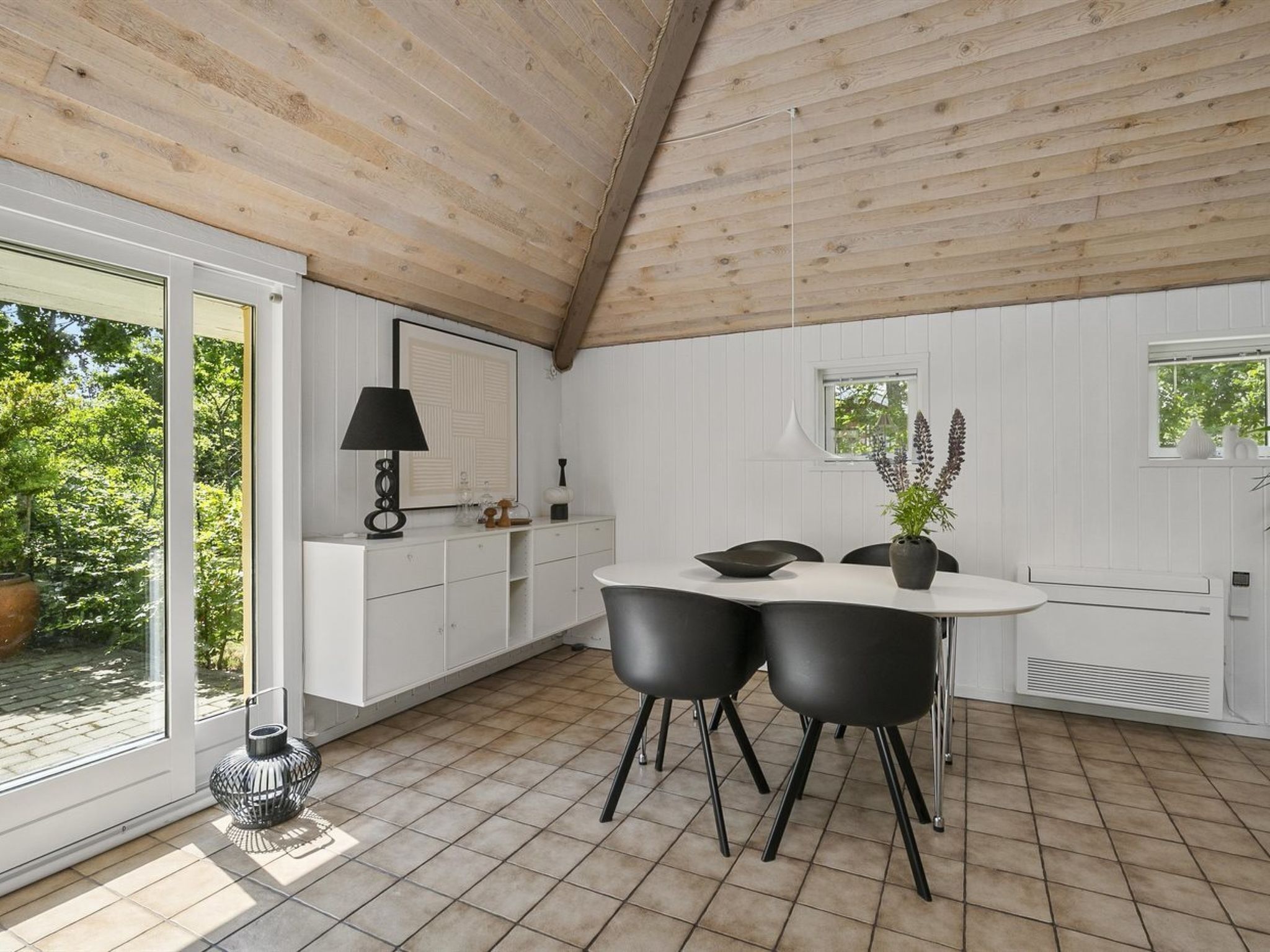 Une cuisine moderne avec un intérieur blanc, un plafond en bois et un coin repas avec des chaises noires.