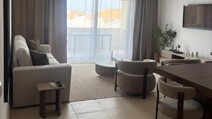 Un salon moderne comprenant un canapé, une table à manger, des chaises, une petite table d’appoint et une grande fenêtre avec des rideaux.