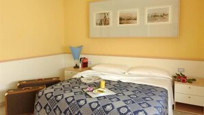 A hotel room with a bed, a nightstand, a lamp, a framed picture on the wall, and a small table with a flower. - Hotel Valverde & Residenza (Cesenatico)
