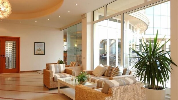 Een moderne lobby met rieten meubels, een bijzettafeltje en een grote potplant.