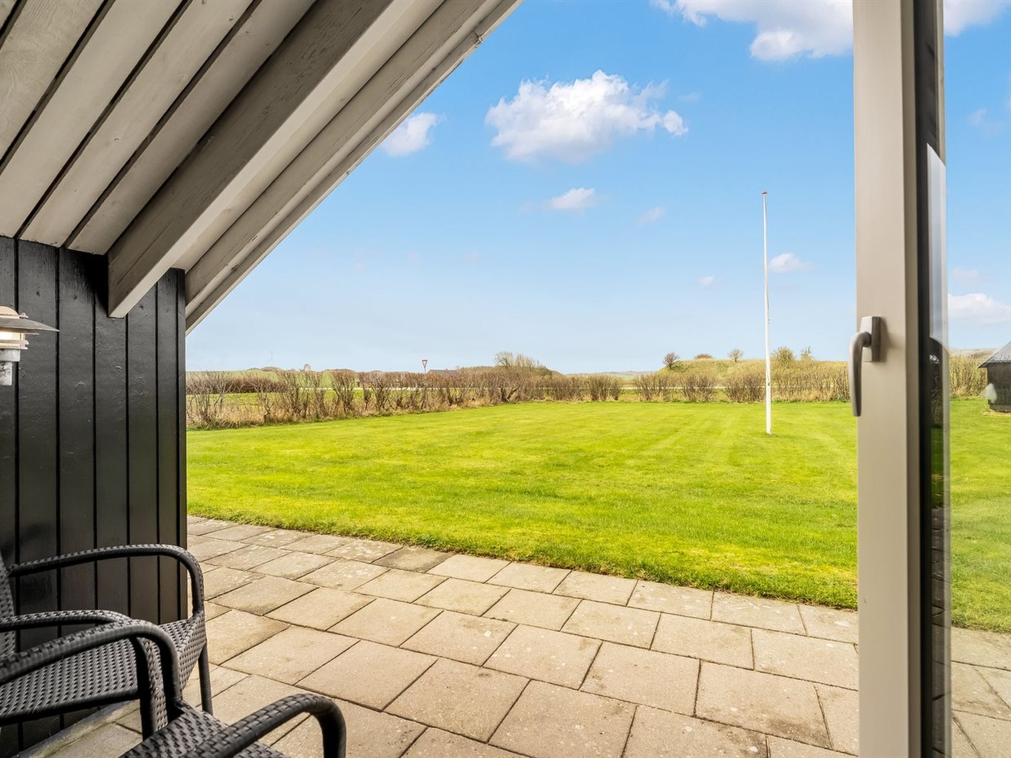 Une terrasse couverte avec vue sur un champ verdoyant et un bâtiment situé au loin.