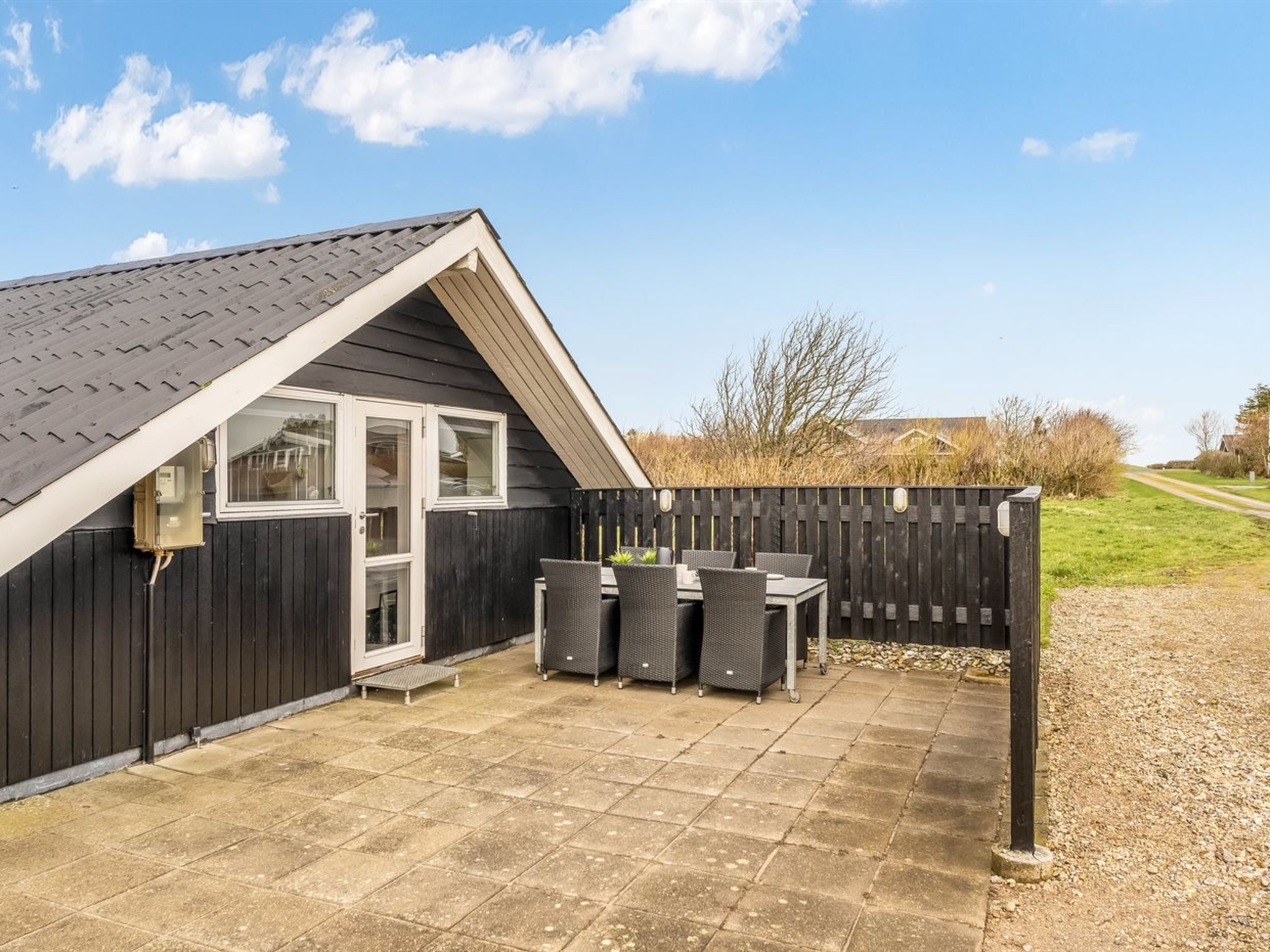 A house with a dark exterior, a sloped roof, and a patio area with a table and chairs.