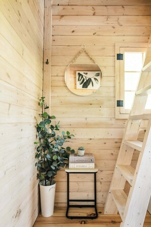 A wooden cabin interior with a plant, a small table with books, and a ladder. - Off-Grid Getaway | Fireplace, BBQ & Patio (Gravenhurst)