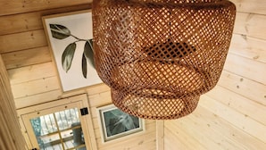 Een houten chaletinterieur met een geweven lamp, een beklede bank, een patroonrijk vloerkleed en een radiator.