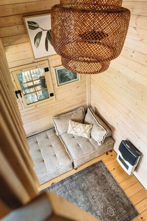 A wooden cabin interior with a woven light fixture, a cushioned bench, a patterned rug, and a radiator. - Off-Grid Getaway | Fireplace, BBQ & Patio (Gravenhurst)