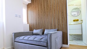 Ein modernes Zimmer mit einem grauen Sofa, einer Wand aus Holzlatten, einem weißen Heizkörper und einem Badezimmer mit Marmorplatte.