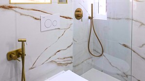 Ein Badezimmer mit Toilette, einer Dusche mit Duschbrause und Marmorwänden.