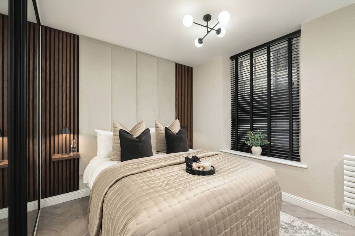Een moderne slaapkamer met een groot bed, een nachtkastje met een lamp, een raam met zonwering en een plafondlamp.