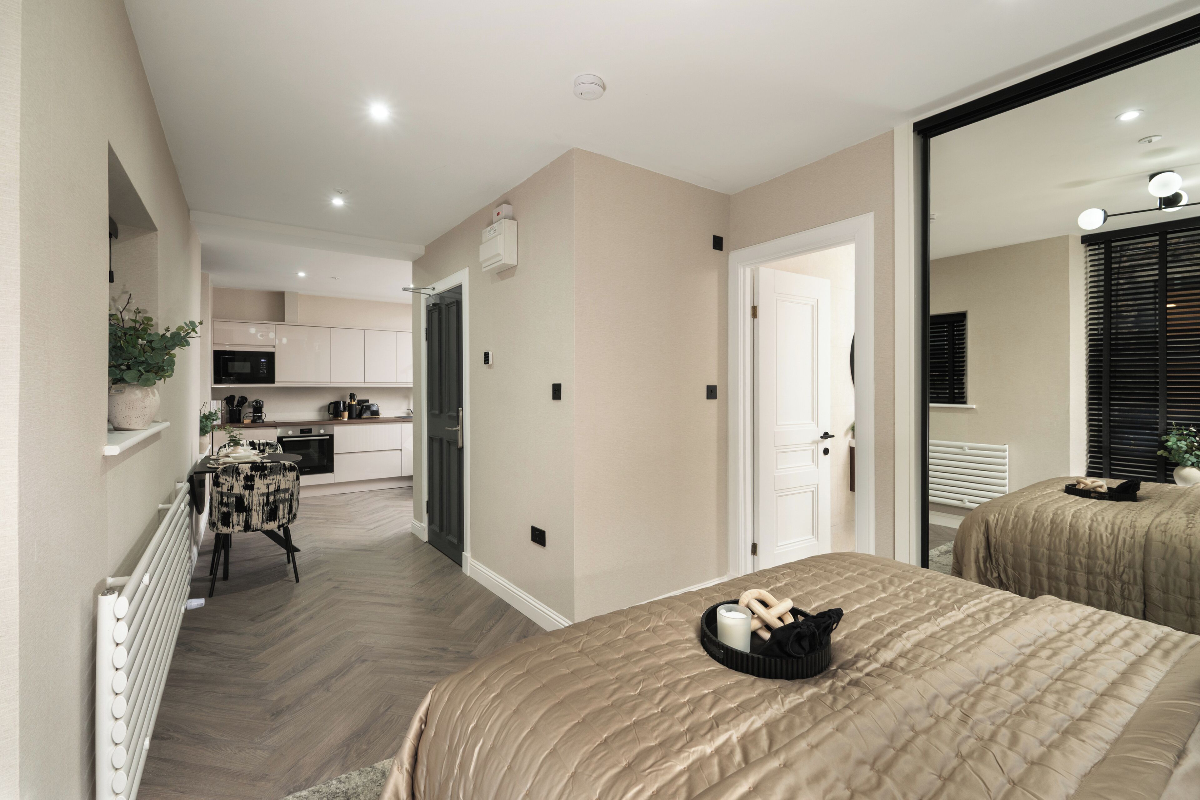 A modern hotel room with a large bed, a dining area, and a kitchen in the background.