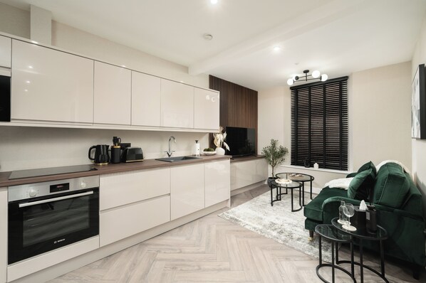 A modern kitchen with white cabinets, a Bosch oven, a sink, and a window with blinds. - South Lane Apartments - City Centre (Edinburgh)