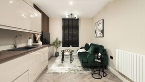Eine moderne Küche mit Spüle, Arbeitsplatte und einer Topfpflanze. Es gibt ein grünes Sofa und einen kleinen runden Tisch mit einem Glas.