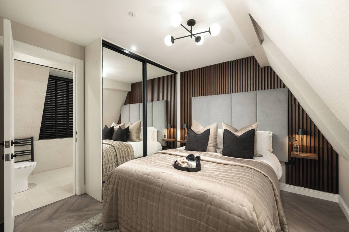 Een slaapkamer met een groot bed, een spiegel, een nachtkastje en een ingebouwde bank.