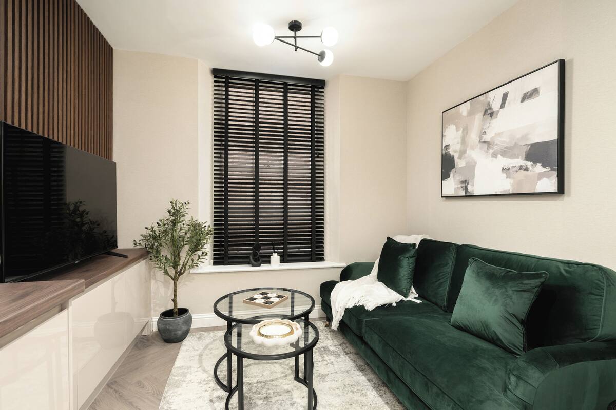 Een moderne woonkamer met een donkergroene bank, een flatscreentelevisie, een kamerplant en een eigentijds abstract schilderij.