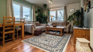 Ett vardagsrum med trägolv, två soffor, ett soffbord, en trästol, ett sidobord och ett stort fönster med gardiner.