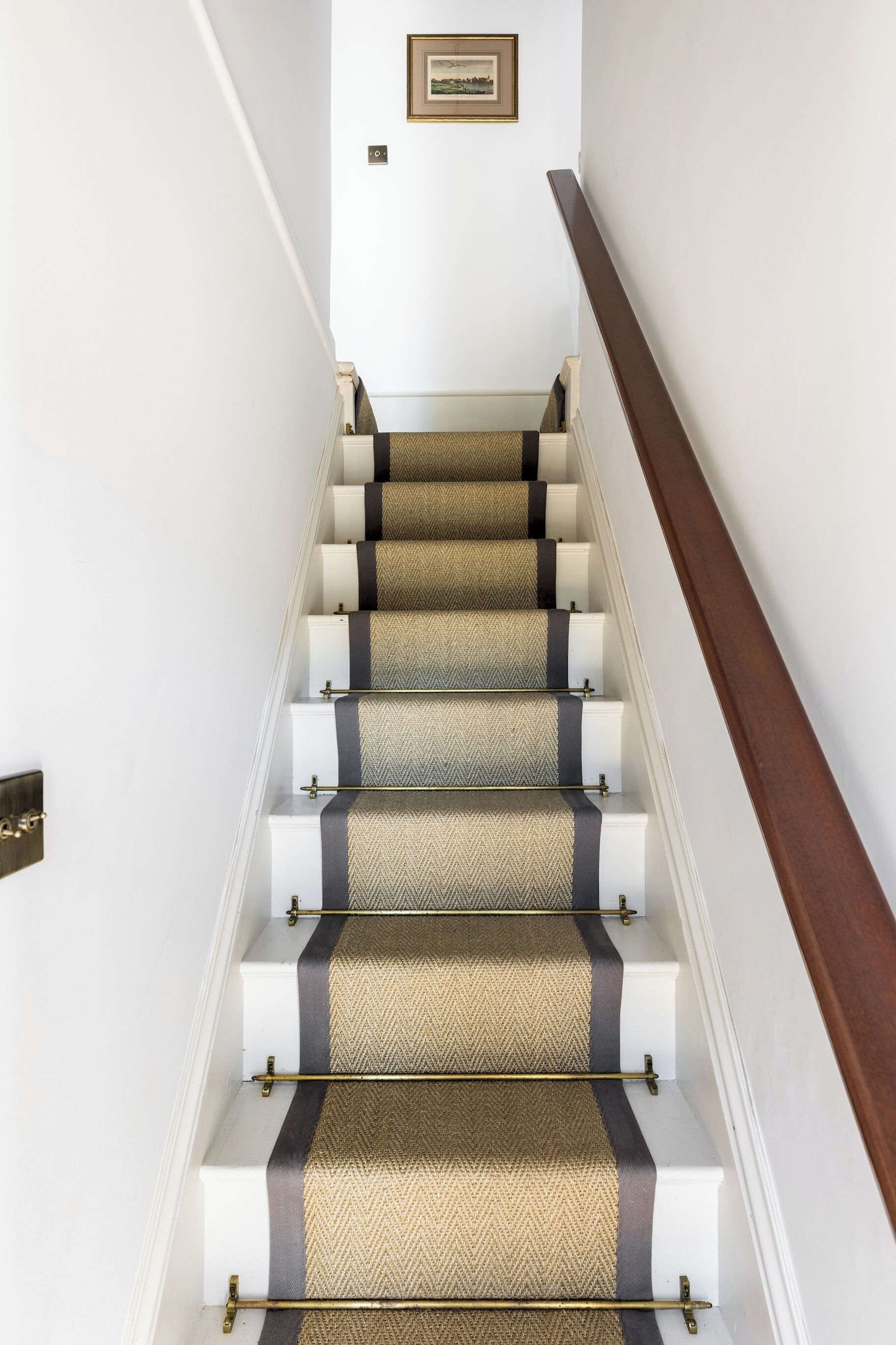 A staircase with patterned carpet and white steps, leading to a landing with a framed picture.