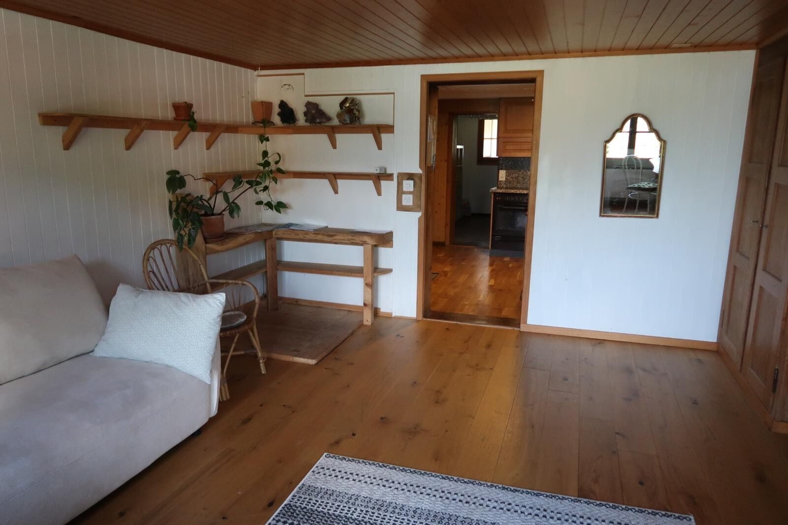 A room with a wooden floor, a sofa, a chair, a small table, and shelves with decorative items.