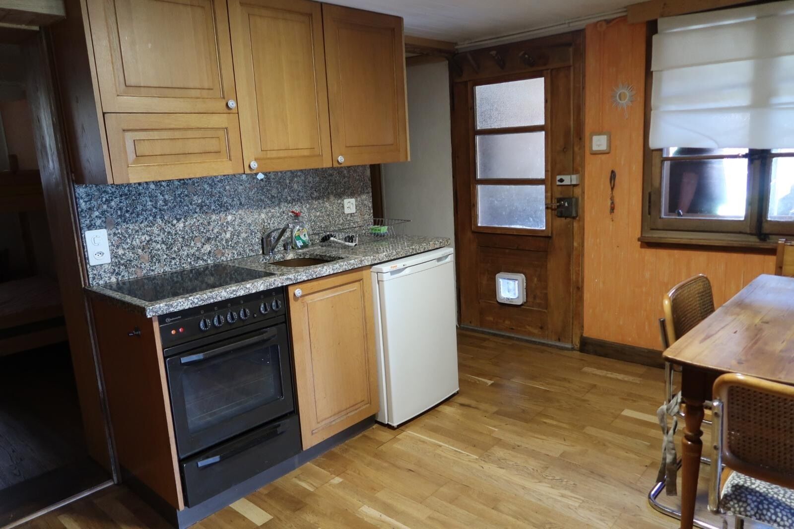 Una cocina con armarios de madera, encimera de granito, horno empotrado, lavavajillas y comedor con mesa y sillas.