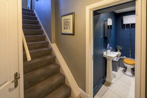 Eine Treppe führt zu einem Badezimmer mit Waschbecken, Toilette und einem gerahmten Bild an der Wand.