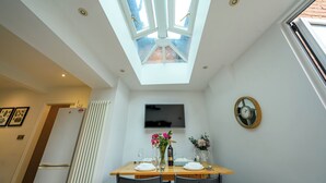 A dining area with a table set for two, a flat-screen TV mounted on the wall, and a skylight above. - Charming 2-Bed Townhouse with Parking, Near Centre - Pass the Keys (Shrewsbury)