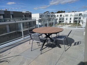 Kattoterassilla on pyöreä puupöytä ja metallituolit, ja sieltä avautuu näkymä modernien rakennusten reunustamalle asuinalueelle.