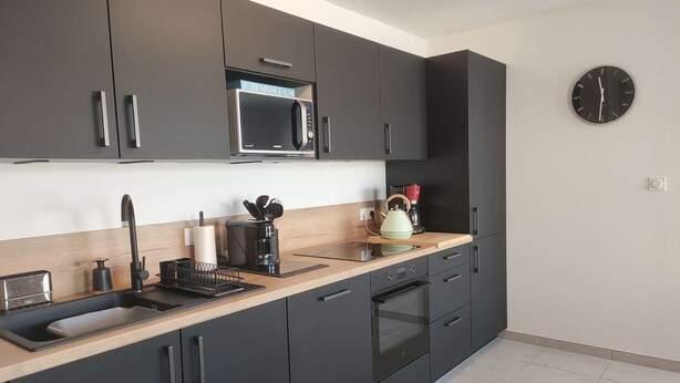 Una cocina moderna con armarios oscuros, un microondas, un hervidor y una cafetera.