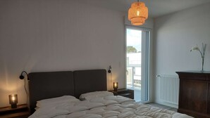 Un dormitorio con cama, lámparas de noche, una ventana y un radiador.