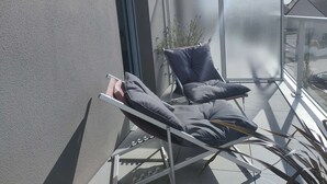 Un balcón con una silla plegable, una planta en maceta y una barandilla de vidrio.