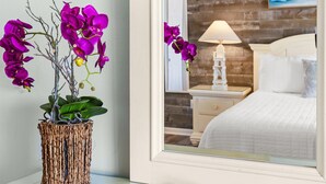 Een slaapkamer met een bed, nachtkastje, lamp en spiegel die de kamer weerspiegelt.