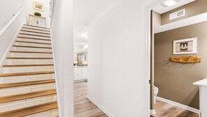 Een trap leidt naar een keuken met witte kasten, een houten kast en een wandplank.