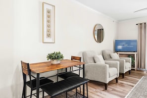 Un salon avec une table en bois, deux bancs noirs, un canapé gris, un téléviseur et un miroir au mur.