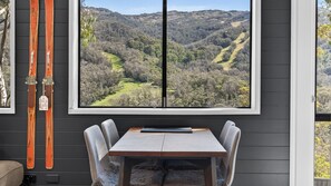 Ein Zimmer mit großem Fenster und Blick auf eine gebirgige Landschaft, einem Holztisch und zwei Stühlen.