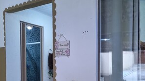 Huone, jossa on laatoitettu suihku, koristeellisella kehyksellä varustettu ovi, verhoilla varustettu ikkuna ja kyltti, jossa on viesti.