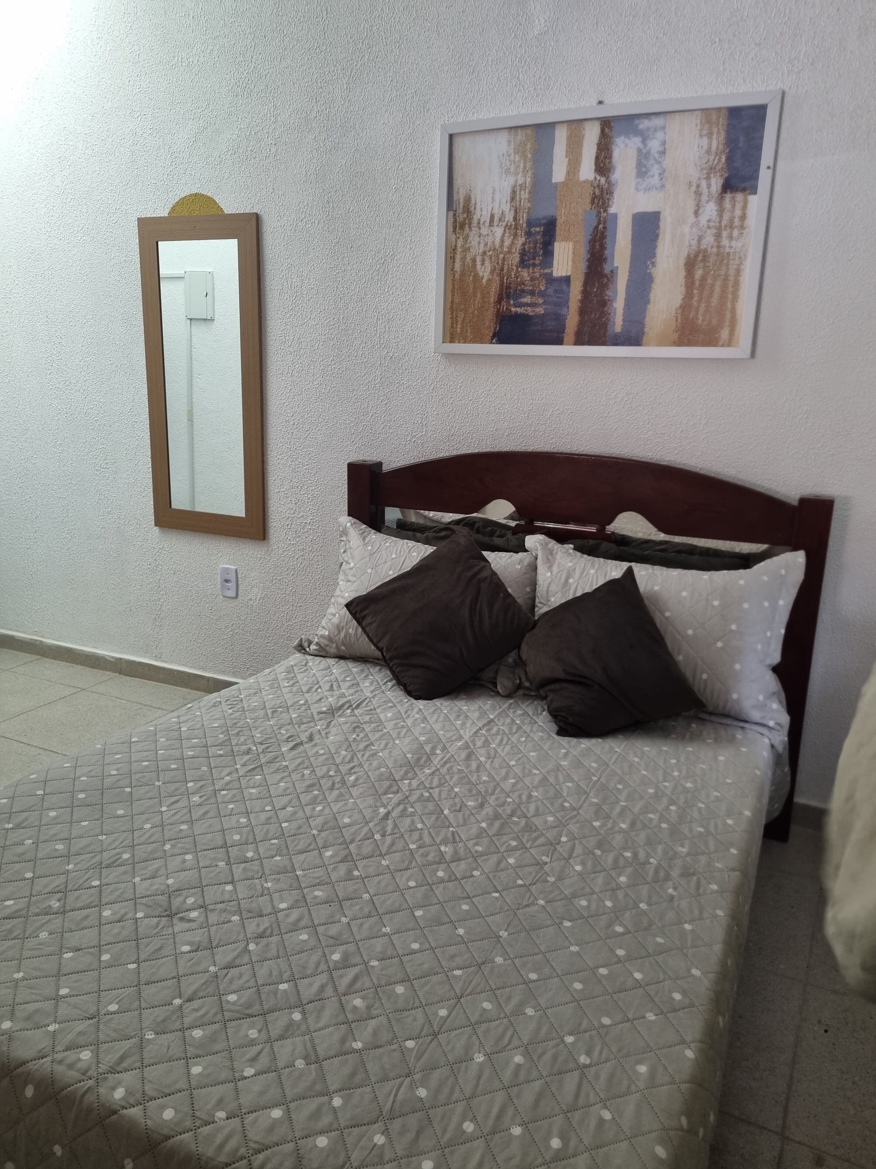 A bed with a quilted cover, a wooden headboard, and several pillows.