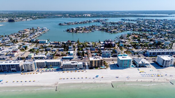 An aerial view of a coastal town with beachfront hotels, a marina, and a clear view of the ocean. - Cottage Pool Across From the Beach (Madeira Beach)