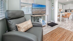 A modern living room with a grey sofa, a television, and a view of the beach through the window. - Cottage Pool Across From the Beach (Madeira Beach)