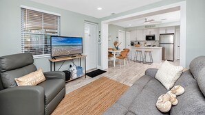 A modern living room with a sofa, TV, and a dining area in the background. - Cottage Pool Across From the Beach (Madeira Beach)
