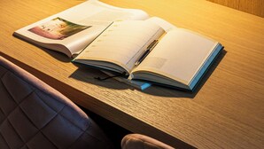 Ein Schreibtisch mit offenem Buch, einer Lampe und einem Stuhl.